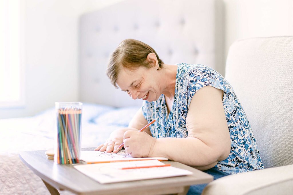 Woman sitting at a table in her bedroom and coloring a color book